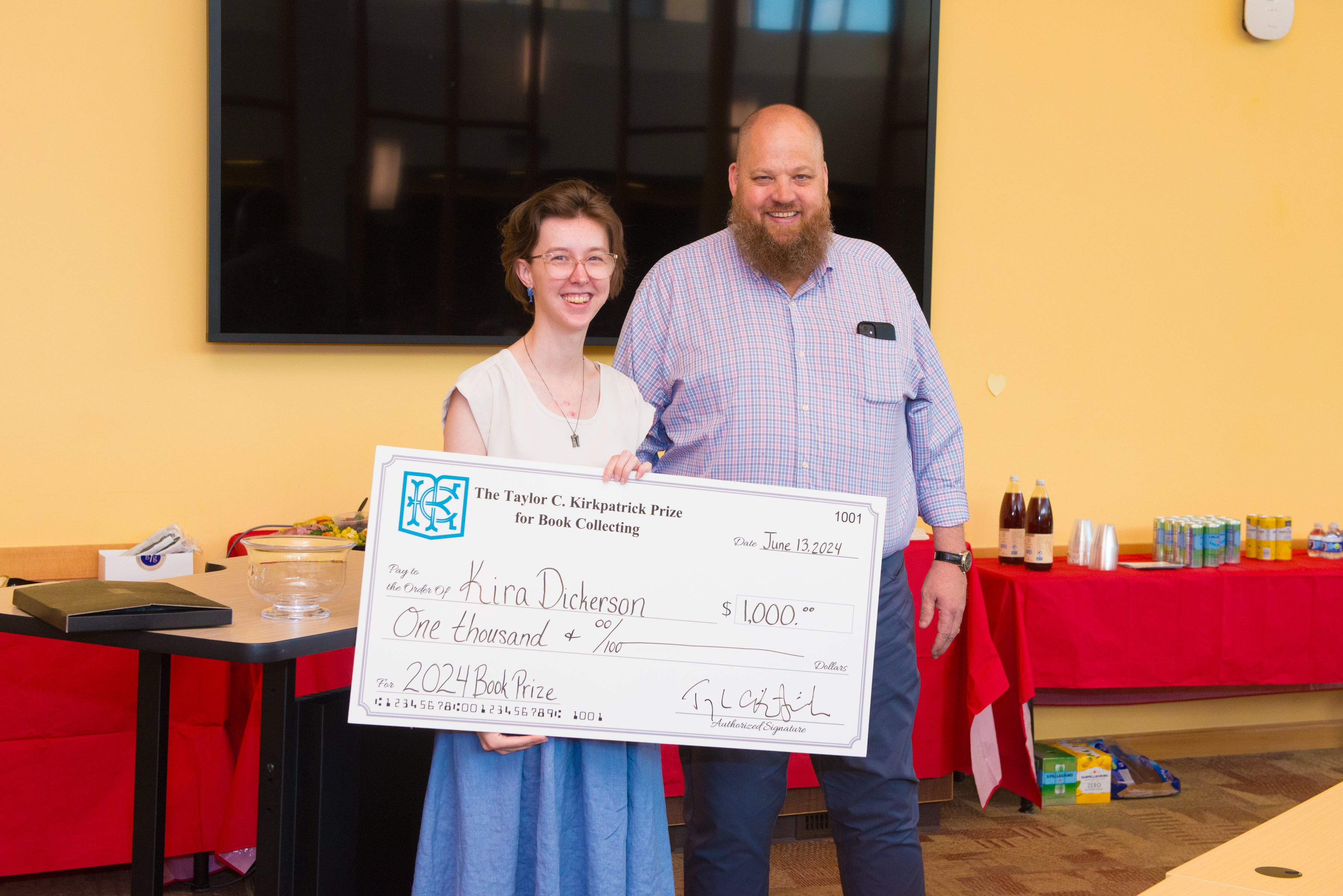 Taylor Kirkpatrick and 2024 Kirkpatrick Book Collecting Prize winner Kira D. stand holding a check with Kira's prize winnings.