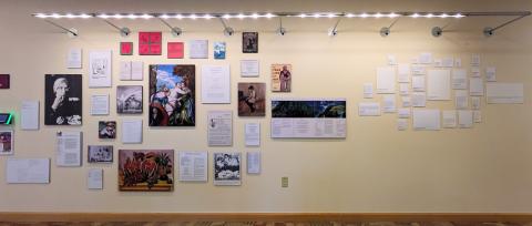 (Image of one wall of the exhibit with a gallery wall of art and recipes)